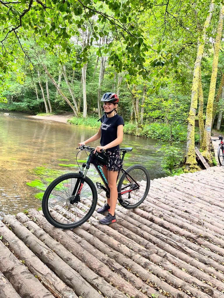 Kobieta z rowerem elektrycznym na moście z bali nad rzeką w lesie