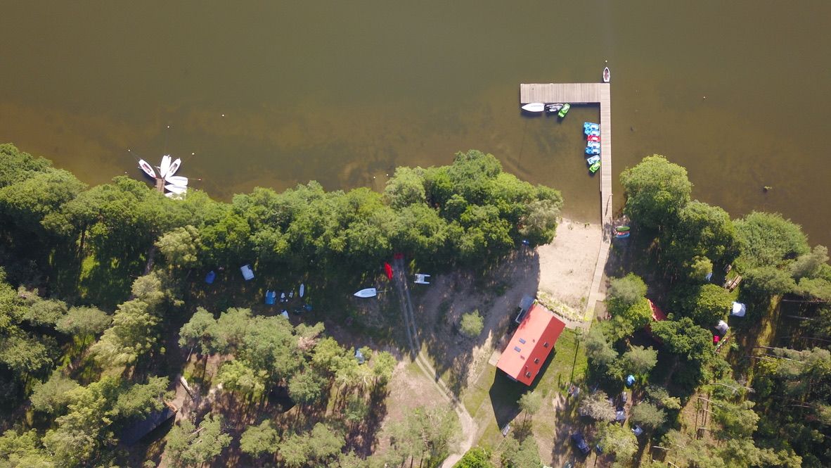 Baza kajakowa z czerwonym budynkiem i molem na brzegu jeziora, widok z drona