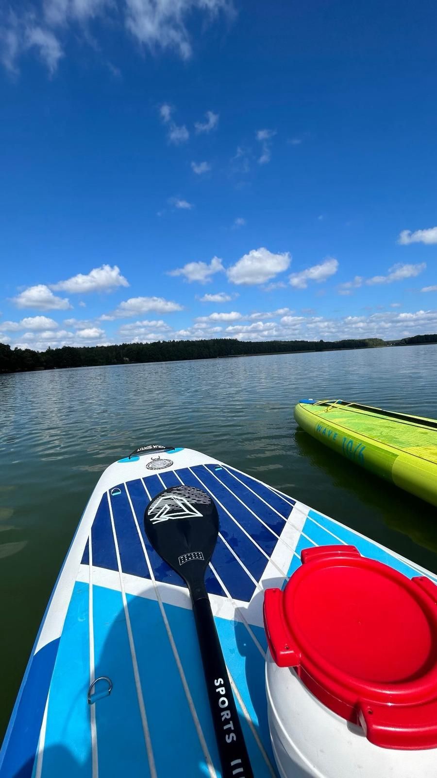 Deski SUP z wiosłem na spokojnym jeziorze, błękitne niebo z chmurami