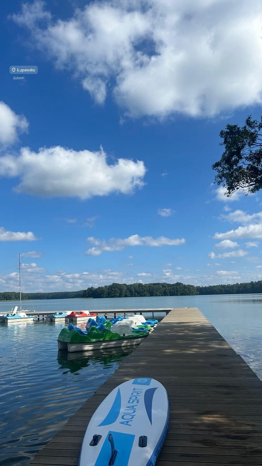 Deska SUP na drewnianym molo z łódkami pedalowymi przy jeziorze