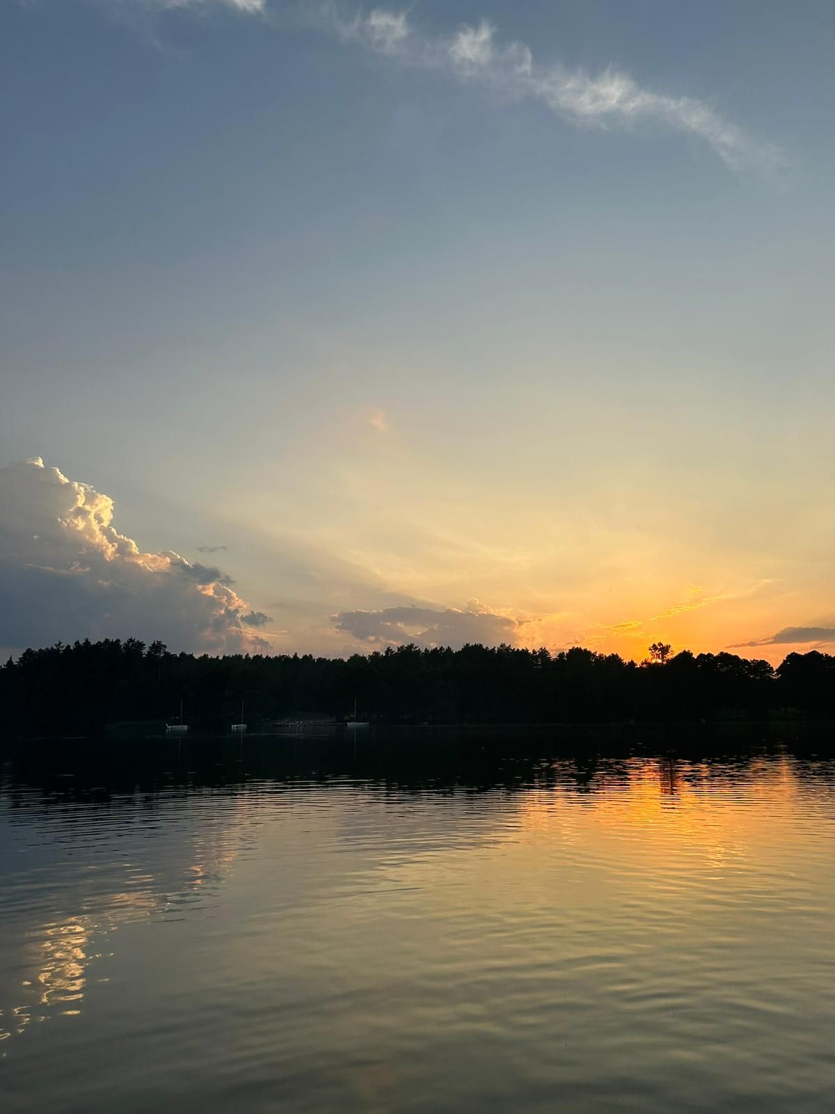 Zachód słońca nad jeziorem z odbiciem w wodzie, las na horyzoncie