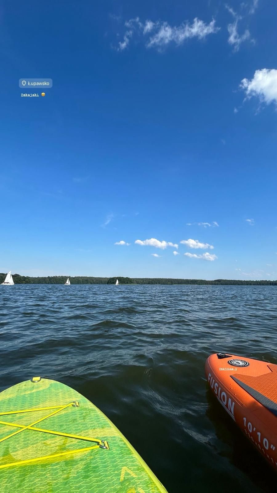 Deski SUP na jezioru z żaglówkami w tle, słoneczny dzień