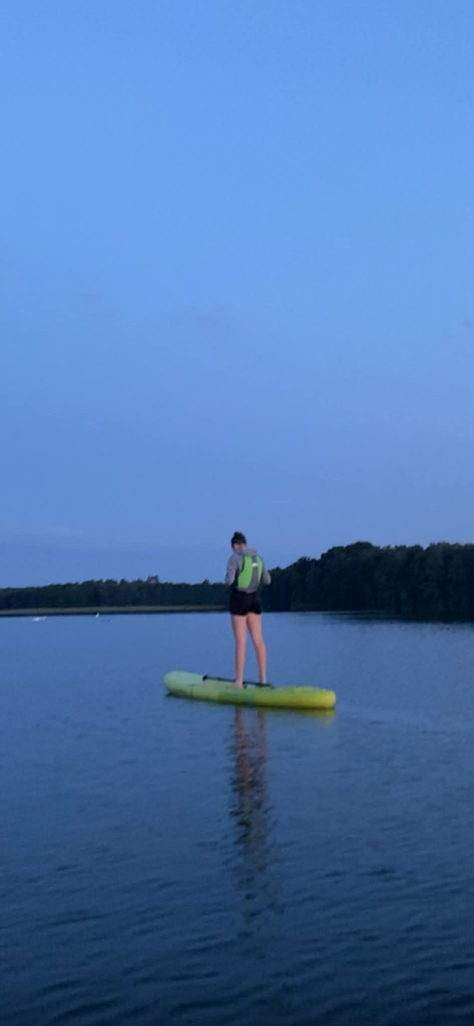 Kobieta na paddleboardzie o zmierzchu, spokojna tafla wody